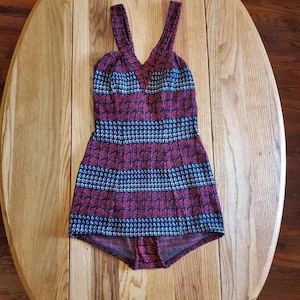May include: A vintage one-piece swimsuit with a red, white, and blue floral pattern. The swimsuit has a V-neck and thin straps.