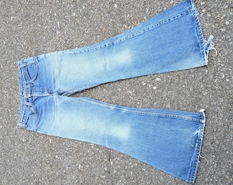 May include: A pair of medium-wash blue denim jeans featuring a flared leg silhouette, a classic five-pocket design, a button and zipper fly closure, and frayed, raw-edge hems at the bottom of each leg, showcasing a faded finish on the thighs.