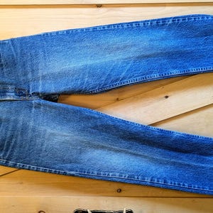 Puede incluir: Un par de pantalones vaqueros azules de mezclilla con piernas remangadas. Los vaqueros tienen un estilo clásico de pierna recta y están hechos de una tela suave y cómoda.