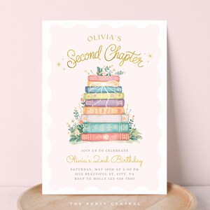 May include: A pink invitation card with gold lettering and a watercolour illustration of a stack of books. The text says "Olivia's Second Chapter" and "Olivia's 2nd Birthday". Floral details and a decorative border are included.