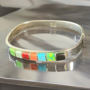 May include: A silver hinged bracelet featuring a series of colourful rectangular inlays. The inlays are made of green, red, orange, turquoise, yellow-green, and black stones. The bracelet has a square shape and a clasp closure.