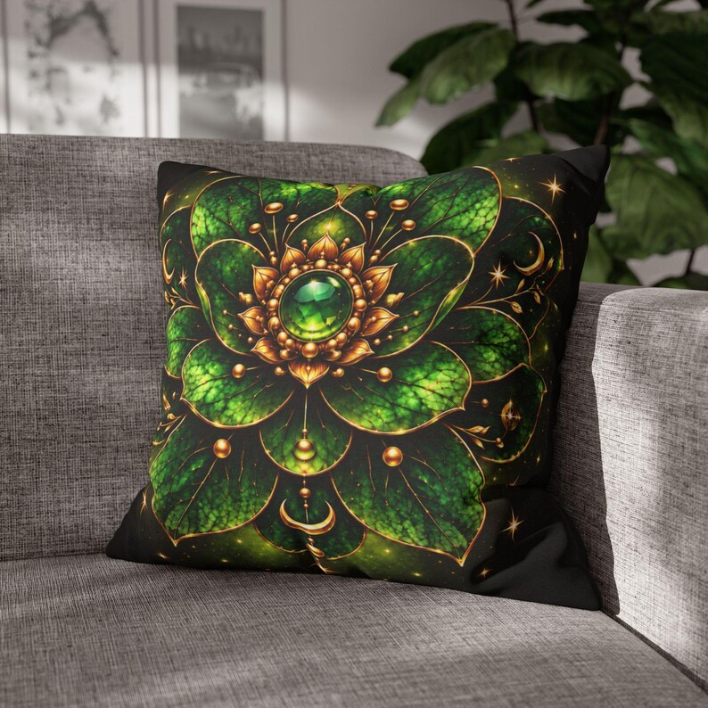 May include: A square throw cushion featuring a black background with a central green and gold mandala-style floral design. The pattern includes layered green leaves, gold accents, small spheres, and a prominent green gemstone at the centre.