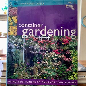 May include: A hardcover book titled "Container Gardening" by Anthony Atha. The cover features a vibrant image of a garden with colorful flowers and greenery. The subtitle reads "Using Containers to Enhance Your Garden."