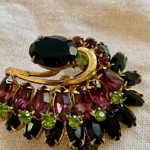 Vintage brooch or pendant in shades of purple and green rhinestones with foiled gold tone backing.