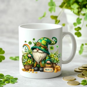 May include: White ceramic mug featuring a St. Patrick's Day gnome with a green hat and plaid jacket. The gnome holds a basket of flowers and a sign that says "March". Gold coins and a rainbow are also depicted.