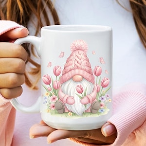 May include: A white ceramic mug with a black handle and the text "But First, Coffee" in a black, bold font. The mug is on a white surface.