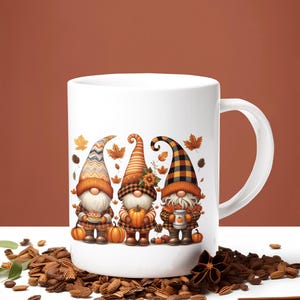 May include: White ceramic mug featuring three autumn gnomes with orange and brown hats and outfits. Each gnome holds a pumpkin, pie, or a mug. The design includes fall leaves and pumpkins, perfect for the autumn season.