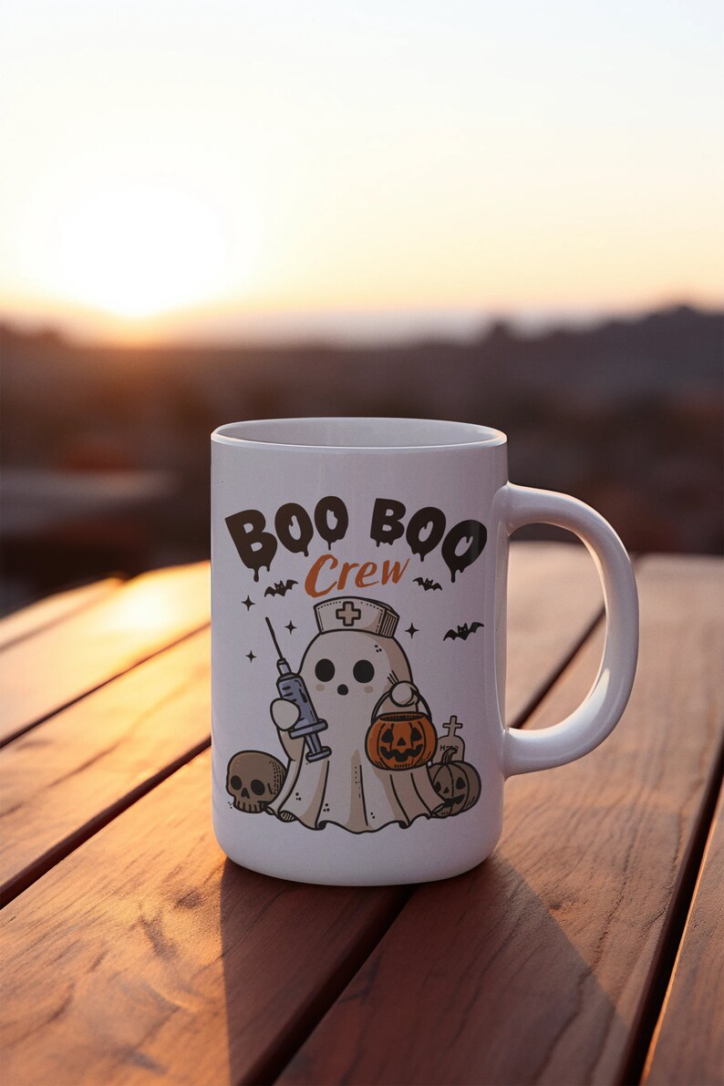 Op de afbeelding: Een witte keramische mok met een zwart-witte illustratie van een spook dat een verpleegstersmuts draagt en een spuit en een pompoen vasthoudt. De tekst "BOO BOO Crew" is in zwart op de mok gedrukt.