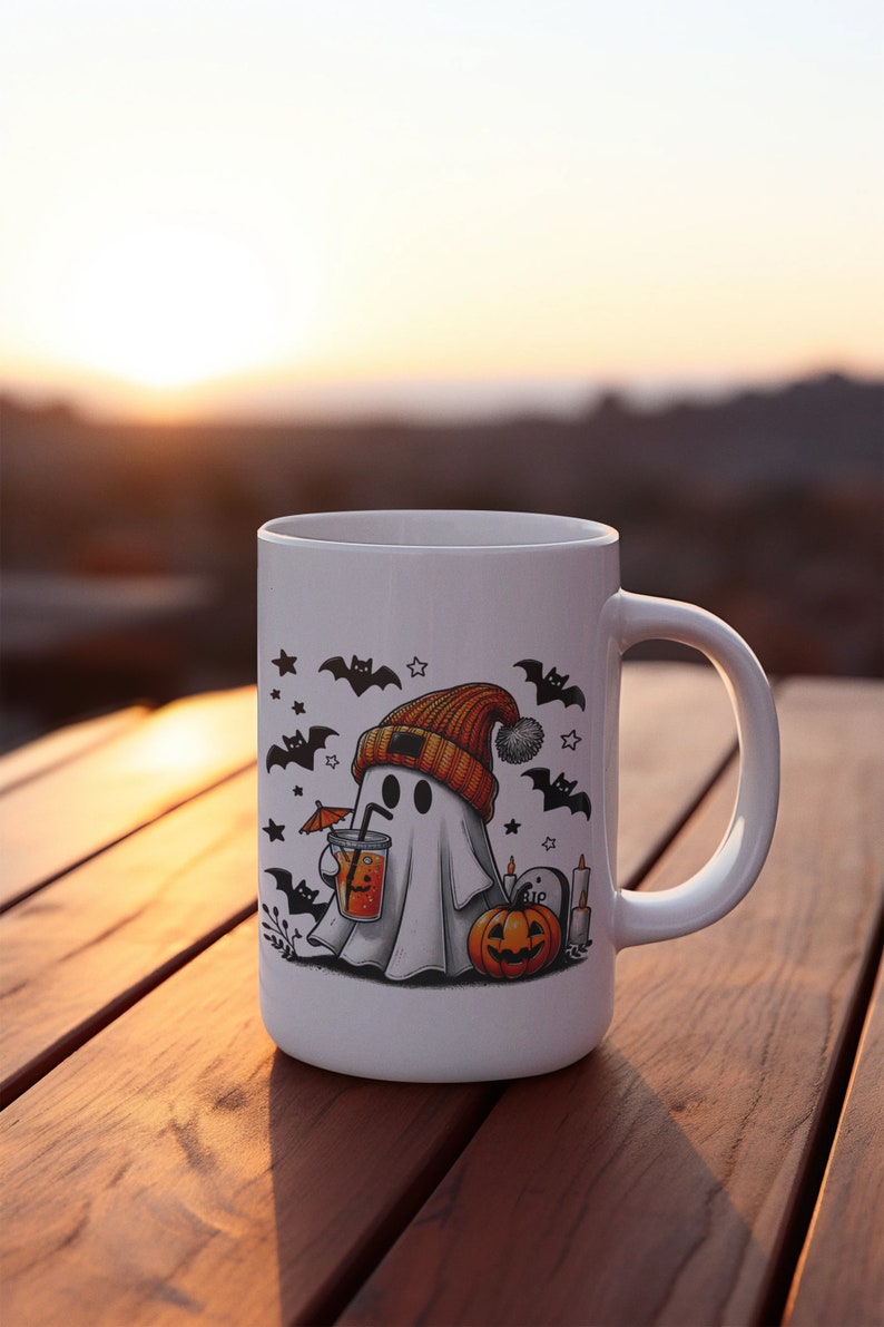 May include: White ceramic mug with a Halloween-themed design. A ghost wearing a beanie hat holds a glass of orange juice. Bats, stars, and a pumpkin are also featured on the mug.