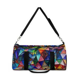 May include: A colorful duffel bag with a geometric stained-glass pattern. The bag features a black shoulder strap and handles. The design includes triangles in shades of blue, green, red, and yellow. The bag is designed for travel or gym use.