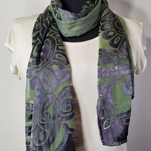 May include: A green and black silk scarf with a paisley pattern. The scarf is folded and draped over a white mannequin.