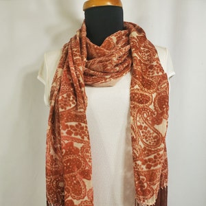 May include: A brown and cream paisley patterned scarf with fringe on the ends.
