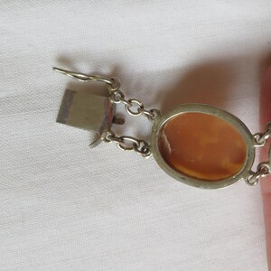 May include: A silver-toned bracelet with oval cameo pendants. The bracelet features a clasp and chain links. The cameo pendants have a light brown color and are set in a silver-toned metal frame. The bracelet is on a white surface.