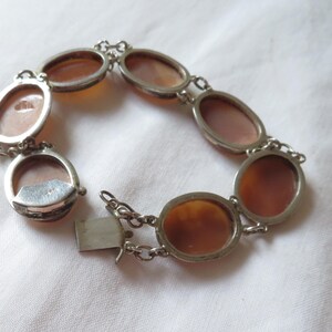 May include: Silver-toned bracelet featuring oval cameo stones in shades of brown and peach. The bracelet has a chain link design with a clasp closure. The cameos are set in silver-toned metal frames.