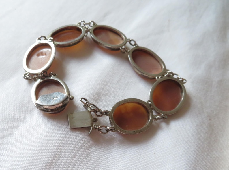 May include: Silver-toned bracelet featuring oval cameo stones in shades of brown and peach. The bracelet has a chain link design with a clasp closure. The cameos are set in silver-toned metal frames.