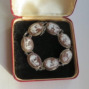 May include: A vintage cameo bracelet with oval-shaped brown and white carved stone settings. The bracelet is set in a silver-toned metal and is displayed in a red velvet lined jewelry box.
