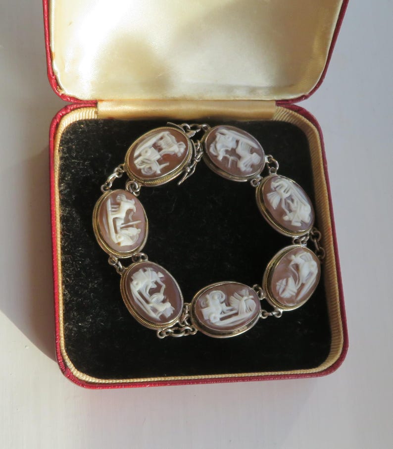 May include: A vintage cameo bracelet with oval-shaped brown and white carved stone settings. The bracelet is set in a silver-toned metal and is displayed in a red velvet lined jewelry box.