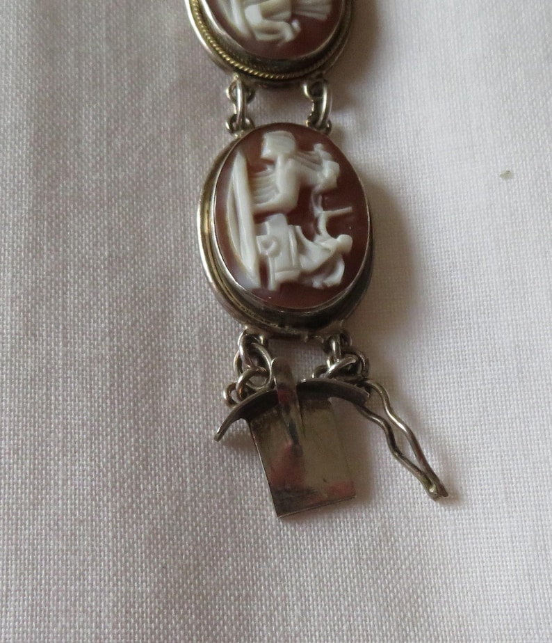 May include: A vintage cameo bracelet featuring oval brown and white carved stone pendants. The bracelet has a silver-toned metal chain and clasp. The cameos depict classical figures.