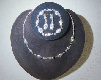 May include: A silver necklace, bracelet and earrings set with clear marquise-shaped stones. The jewellery is displayed on a black velvet background.