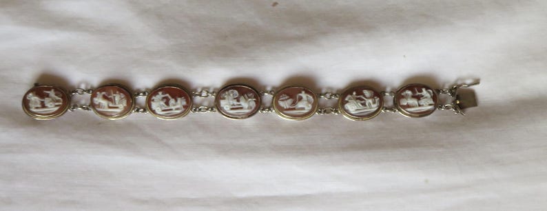 May include: A vintage bracelet featuring oval cameos with white relief figures set in gold-toned frames. The cameos are connected by a delicate silver chain, and the bracelet has a clasp closure. The bracelet is displayed on a white surface.