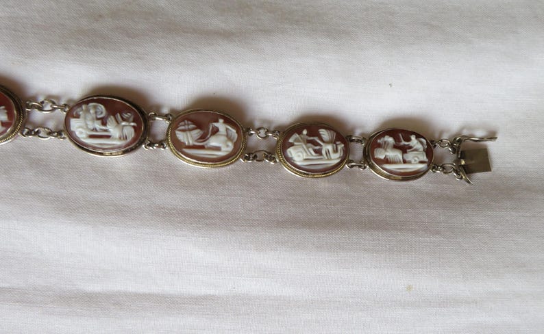 May include: A vintage bracelet featuring oval cameo pendants with white relief figures set in gold-toned frames. The bracelet is connected by delicate silver-toned chains and has a clasp closure. The cameos depict classical scenes.