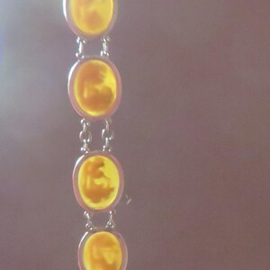 May include: A silver-toned bracelet featuring a series of circular, amber-colored stones. Each stone is connected by small silver links. The stones have a unique, textured appearance, and the bracelet is set against a soft, blurred background.