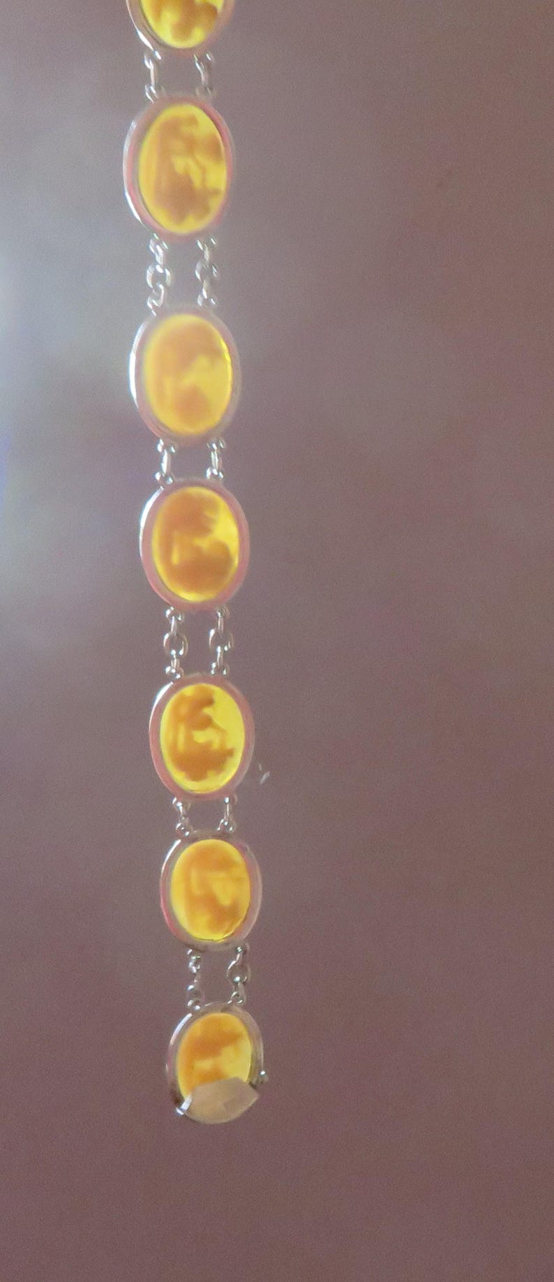 May include: A silver-toned bracelet featuring a series of circular, amber-colored stones. Each stone is connected by small silver links. The stones have a unique, textured appearance, and the bracelet is set against a soft, blurred background.