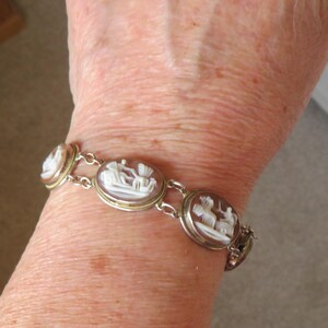 May include: A silver-toned bracelet featuring oval cameos with white relief carvings. The cameos are set in gold-toned bezels and connected by delicate links. The bracelet is worn on a wrist.