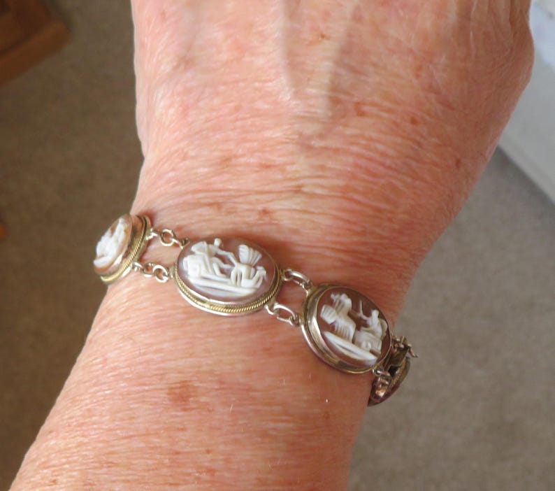 May include: A silver-toned bracelet featuring oval cameos with white relief carvings. The cameos are set in gold-toned bezels and connected by delicate links. The bracelet is worn on a wrist.