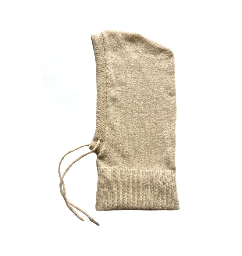 May include: A beige knitted balaclava with a drawstring tie. The balaclava is made of a soft, warm material and is ideal for cold weather.