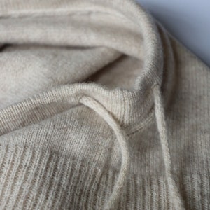 May include: Close-up of a beige knitted jumper with a drawstring hood.