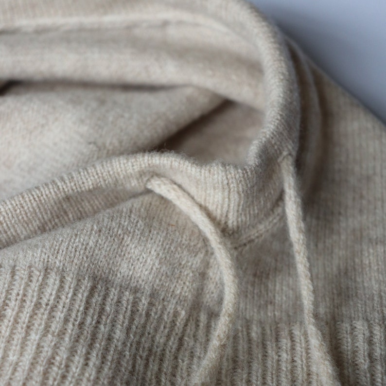 May include: Close-up of a beige knitted jumper with a drawstring hood.