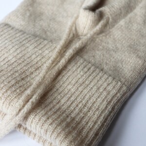 May include: A beige knitted jumper with a ribbed texture. The jumper is folded in half and the neckline is visible.