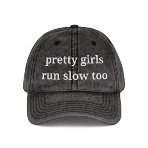 May include: A distressed black baseball cap with the text "pretty girls run slow too" embroidered in white. The cap has a curved brim and an adjustable strap.