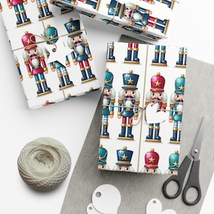 May include: White wrapping paper with a repeating pattern of colorful nutcracker figurines. The nutcrackers are wearing blue and red uniforms with gold accents. The paper is wrapped around a gift box and tied with twine.