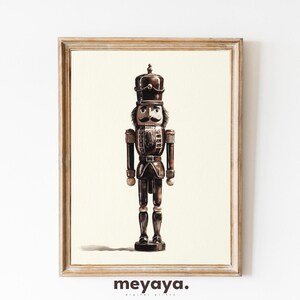 May include: Watercolor print of a traditional nutcracker soldier in a wooden frame. The nutcracker is depicted in shades of brown and black, with a detailed uniform and a distinguished mustache. The print is set against a cream-colored background.