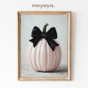 May include: A framed print featuring a pink pumpkin with a black bow. The pumpkin has vertical ridges and a curved stem. The artwork is displayed in a light-colored wooden frame, with the text "meyaya." at the top.