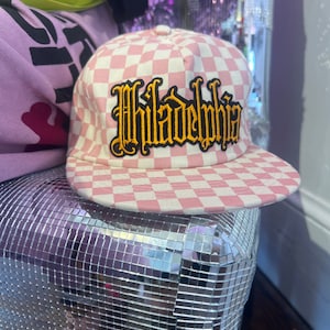 May include: Pink and white checkered baseball cap with a black and yellow embroidered "Philadelphia" logo.
