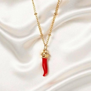 May include: A gold necklace featuring a red chili pepper pendant, crowned with gold. The delicate chain hangs against a white, silky backdrop. The chili pepper pendant is approximately 2.5 cm long. A stylish piece of jewelry.