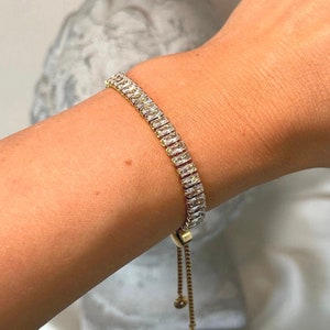 Könnte beinhalten: Ein goldenes Kettenarmband mit einer Reihe von klaren rechteckigen Steinen. Das Armband hat einen verstellbaren Verschluss.