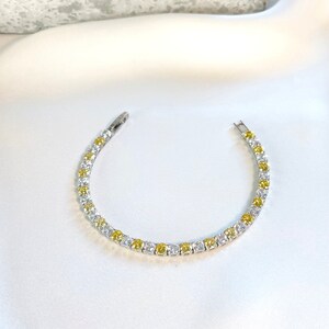 Puede incluir: Un brazalete de tenis de plata con piedras de circonita cúbica transparentes y amarillas alternadas.