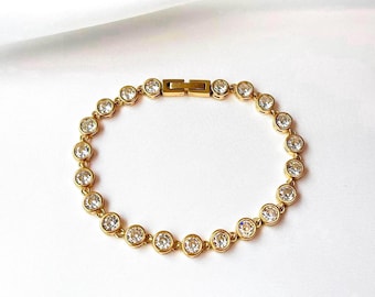 Puede incluir: Un brazalete dorado con una fila de piedras redondas transparentes.