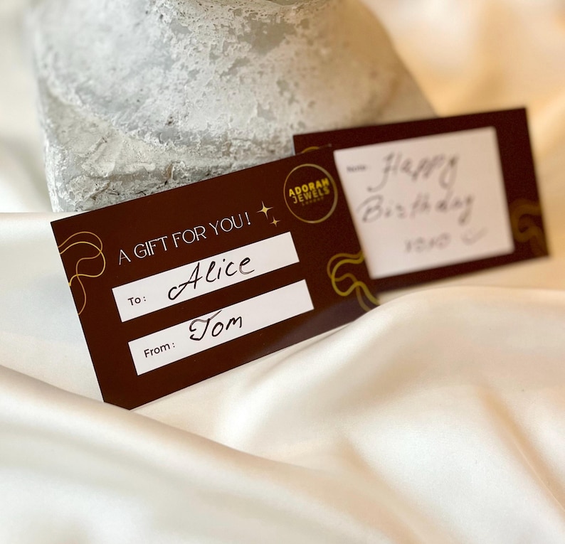 May include: Two gift cards on a white satin surface. One card is brown with gold accents and the text "A GIFT FOR YOU!" and "To: Alice" and "From: Tom". The other card has handwritten text that says "Happy Birthday".