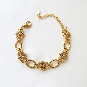 May include: A gold-toned chain bracelet with a delicate, intricate design. The bracelet features a series of linked oval shapes and small, flower-like accents.