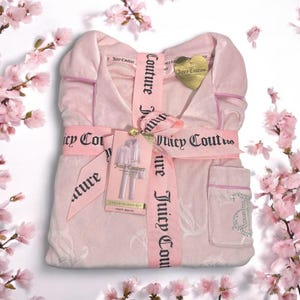 May include: A light pink Juicy Couture 2-piece pajama set, tied with a pink ribbon printed with "Juicy Couture". The set includes a robe and trousers, with a tag that says "2 PIECE PAJAMA SET". The robe has a pocket with the letter "J" embellished with rhinestones.