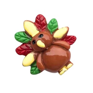 May include: A brown and yellow turkey figurine with red and green leaves for a tail. The turkey has black eyes and a yellow beak.