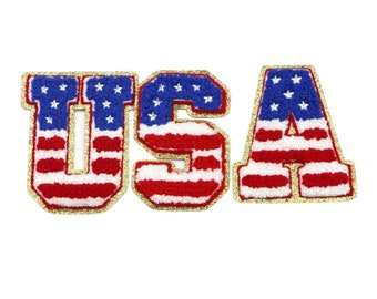 May include: USA spelled out in large, red, white, and blue letters with gold glitter trim. Each letter is decorated with a stylized American flag pattern.