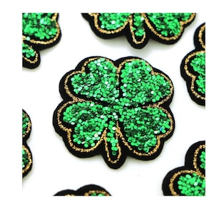 May include: Green sequined four-leaf clover patches with black borders and gold trim. These decorative patches are ideal for adding a touch of sparkle to clothing, accessories, or craft projects. The clover design is a symbol of good luck.
