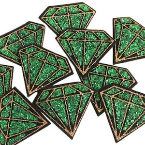 May include: A group of ten green and gold glitter diamond shaped iron-on patches. The patches are arranged in a pile, with some overlapping.