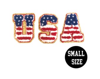 May include: Three felt letters spelling "USA" in a gold outline. Each letter is decorated with a red, white, and blue American flag pattern. The letters are small in size.